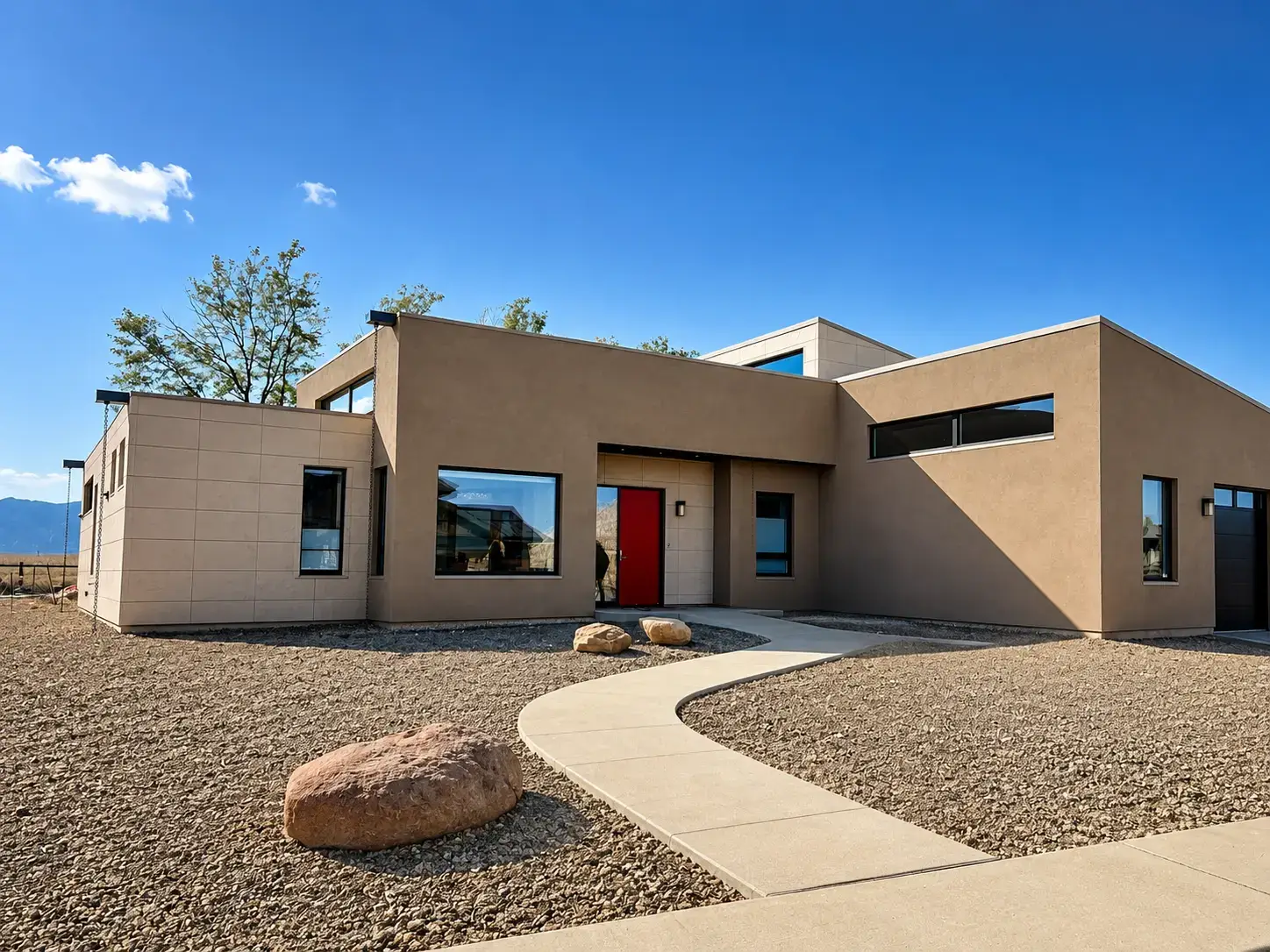 Exterior of the ENCLAVE Louisville Passive House with large black-framed windows, a red entry door and modern stucco facade.